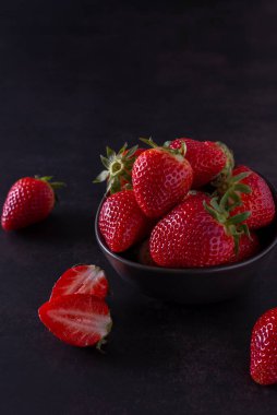 Siyah bir kasede koyu arkaplanı olan çilekler