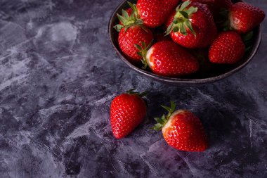 Gri arkaplanlı siyah bir kasede çilekler