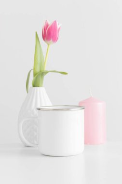 Enamel kupası, vazoda pembe bir lale ve beyaz bir masada mum..