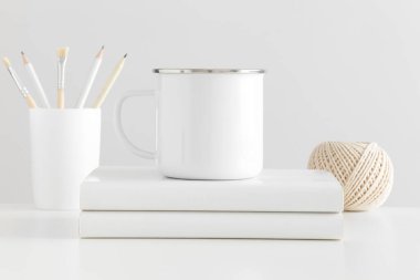 Beyaz bir masa üzerinde çalışma alanı aksesuarları olan Enamel kupası..