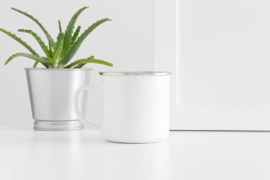 Enamel kupası, çalışma alanı aksesuarları ve beyaz bir masada sulu bir bitki..