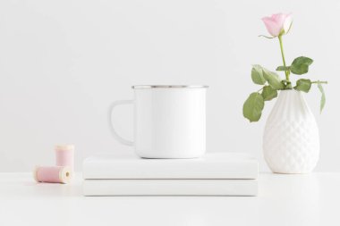 Enamel kupası, pembe bir gül ve beyaz bir masa üzerinde kitaplar..