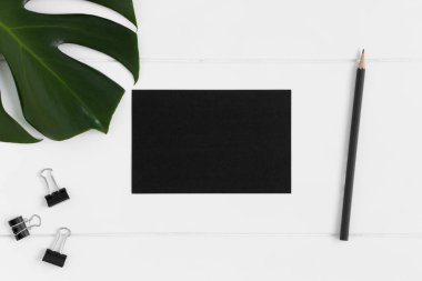 Çalışma alanı aksesuarları ve beyaz masa üzerinde canavar yaprağı olan bir siyah kart modelinin üst görüntüsü.