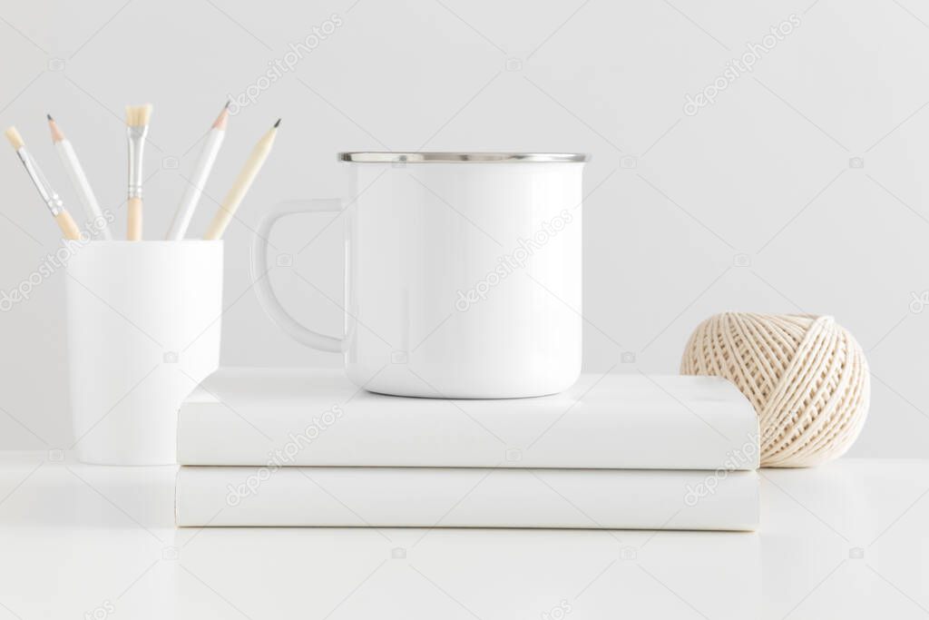 Enamel mug mockup with workspace accessories on a white table.