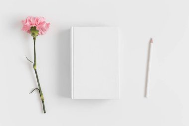 Beyaz bir masanın üzerinde pembe karanfil olan bir kitap modeli..