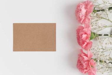 Beyaz bir masada çingene ve pembe karanfilli bir kraft kartının üst görüntüsü..