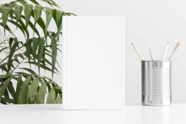 Çalışma alanı aksesuarları ve palmiye bitkisi olan beyaz kitap modeli..