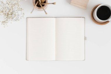 Çalışma alanı aksesuarları olan bir defter modeli ve beyaz bir masadaki vazoda bir çingene resmi..