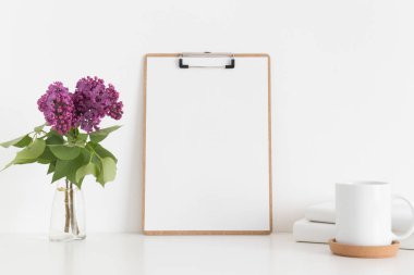 Çalışma alanı aksesuarlarıyla ahşap pano modeli ve beyaz bir masadaki vazoda leylak..