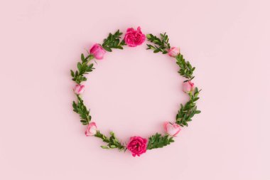 Pembe güllerden ve pembe arka planda yeşil dallardan yapılmış çiçek çelengi..