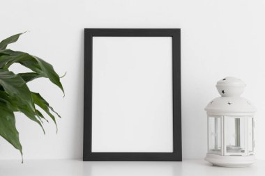 Siyah çerçeve modeli, spathiphyllum ve mum tutacağı beyaz bir masada. Portre yönelimi.