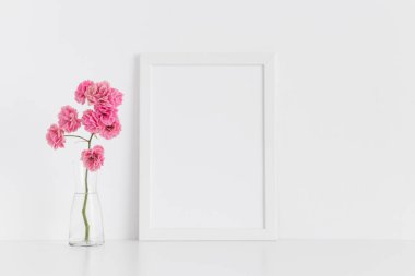 Beyaz çerçeveli, pembe güllü, cam bir vazoda beyaz bir tablo. Portre oryantasyonu..