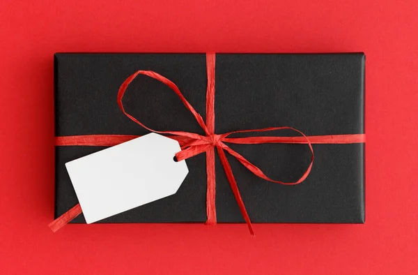 Zwart Kerstcadeau Met Een Blanco Tag Mockup Een Rode Achtergrond — Stockfoto