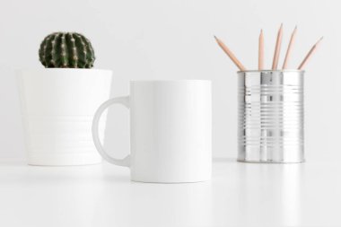 Çalışma alanı aksesuarları ve beyaz masada bir tencerede kaktüs olan kupa modeli..