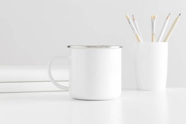 Beyaz bir masa üzerinde çalışma alanı aksesuarları olan Enamel kupası..