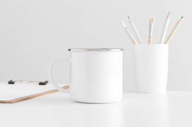 Beyaz bir masa üzerinde çalışma alanı aksesuarları olan Enamel kupası..