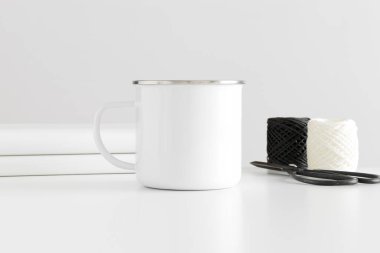 Beyaz bir masa üzerinde çalışma alanı aksesuarları olan Enamel kupası..