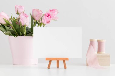 Beyaz kart modeli, ipek kurdeleler ve beyaz bir masada pembe güller..