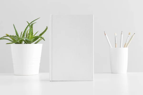 White book mockup with workspace accessories and a succulent plant on a white table.
