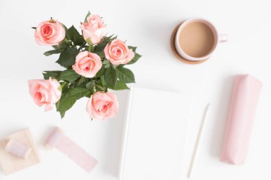 Bir buket pembe gül, kitap, kahve ve çalışma alanı aksesuarları beyaz bir masada. Boş kopya alanı ile düz yatıyordu.