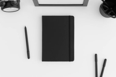 Beyaz bir masada çalışma alanı aksesuarları olan siyah defter modeli.
