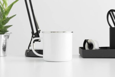 Beyaz bir masa üzerinde lamba, aloe vera bitkisi ve çalışma alanı aksesuarları ile Enamel kupa modeli.