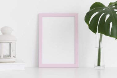 Çalışma alanı aksesuarlarıyla pembe çerçeve modeli ve beyaz bir masada vazoda bir canavar yaprağı. Portre oryantasyonu..