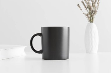 Siyah kupa, vazoda bir lavanta ve beyaz masada bir kitap..