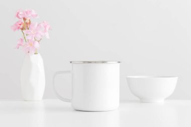 Enamel kupası, vazoda bir buket pembe zakkum ve beyaz bir masada bir kase ile..