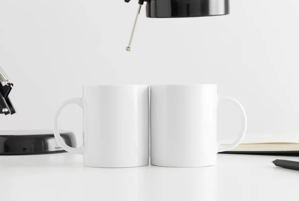 Két Fehér Bögrét Egy Lámpával Egy Noteszral Fehér Asztalon — Stock Fotó