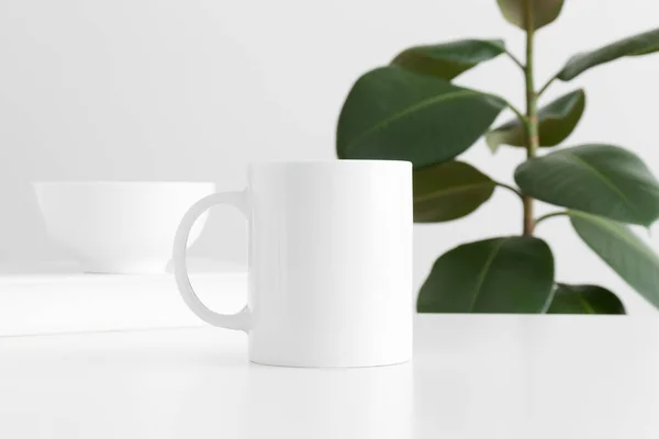 白いテーブルの上のワークスペースの付属品と架空の植物と白いマグカップのモックアップ — ストック写真