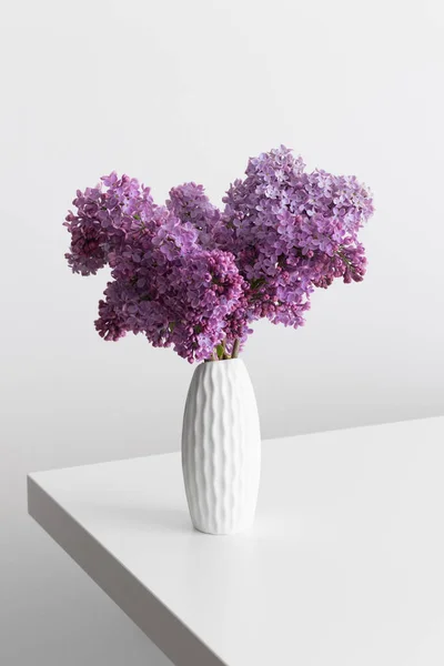Bouquet of lilac flowers in a vase on a white table.