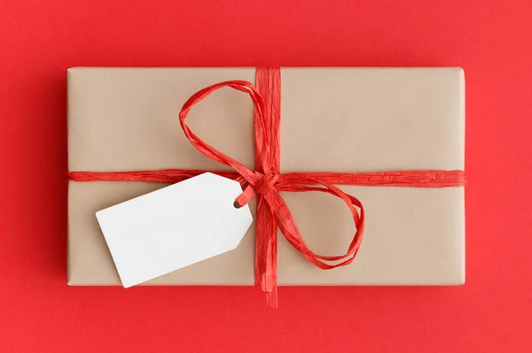 Kraft Kerstcadeau Met Een Blanco Tag Mockup Een Rode Achtergrond — Stockfoto