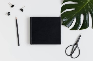 Çalışma alanı aksesuarları ve beyaz bir masada canavar yaprağı olan siyah bir kitap modelinin üst görüntüsü..