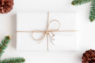 Beyaz bir noel hediyesinin üst görüntüsü. Üzerinde çam kozalakları ve yapraklarla dolu boş bir etiket var..