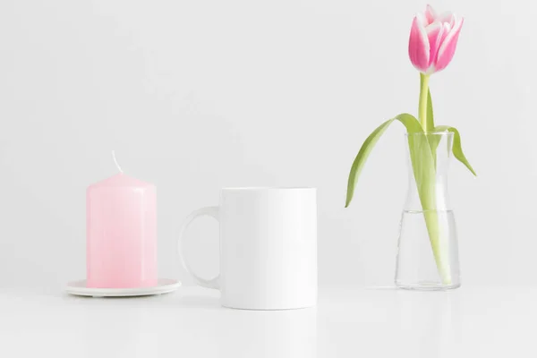 白いテーブルの上に花瓶やキャンドルにピンクのチューリップとマグカップモックアップ — ストック写真