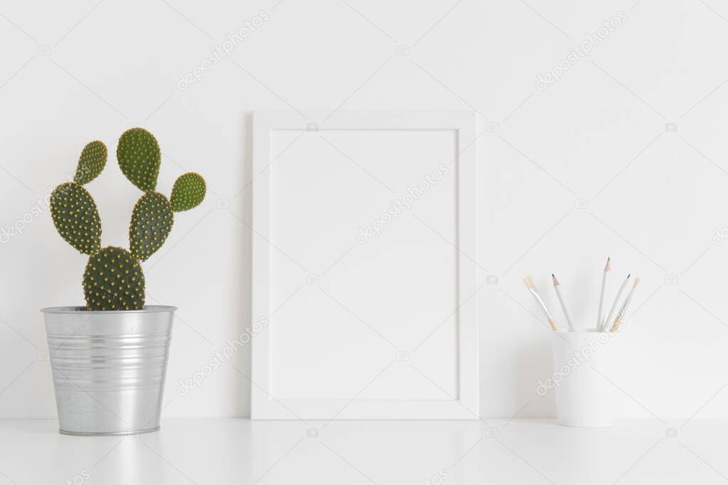 White frame mockup with a cacutus in a pot and workspace accessories on white table. Portrait orientation.