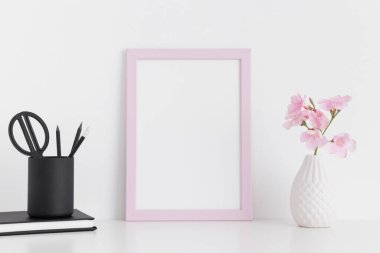 Cam vazoda pembe zakkum ve beyaz bir masa üzerinde çalışma alanı aksesuarlarıyla pembe çerçeve modeli..