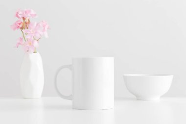 Vazoda bir buket pembe zakkum ve beyaz bir masada bir kase ile beyaz kupa modeli..