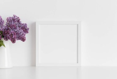 Beyaz kare çerçeve, beyaz bir masadaki vazoda bir demet leylak..