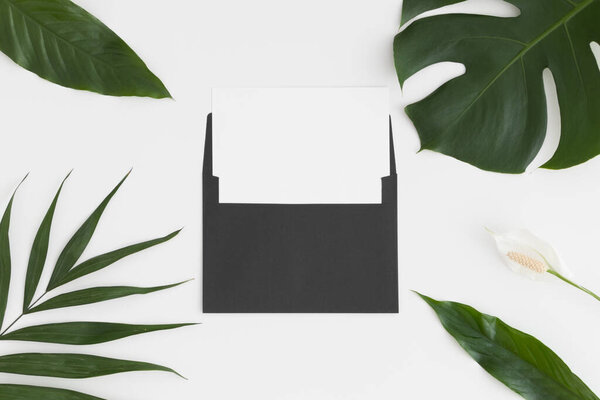 Верхний вид макета белой карты с декорированием тропических листьев на белом столе.