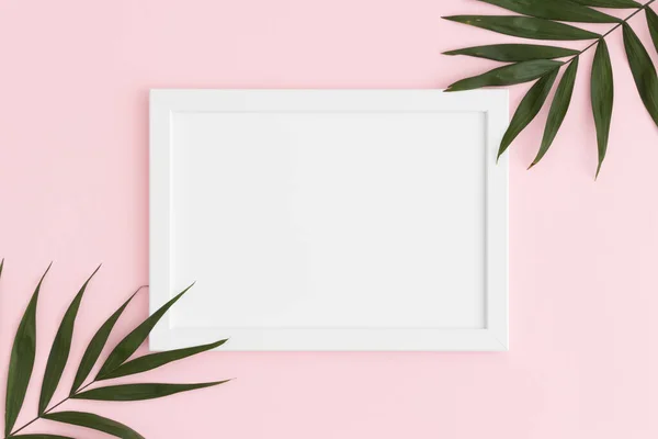Top view of a white frame mockup with palm leaf decoration on a pink background. Landscape orientation.