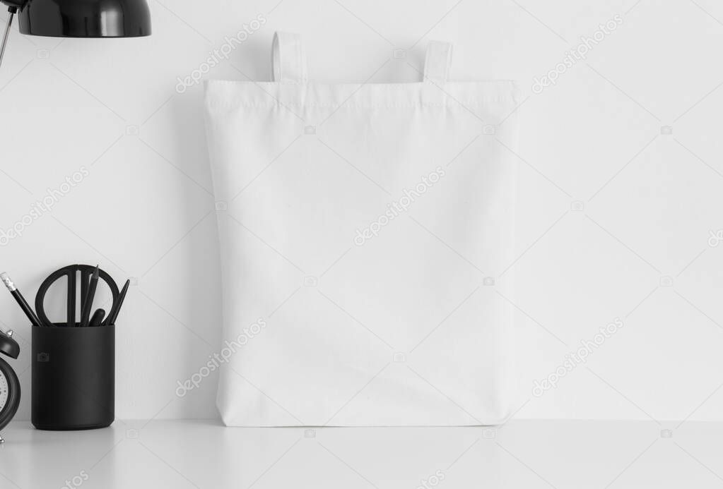 White tote bag mockup with workspace accessories on a white table.