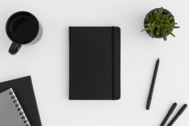 Beyaz bir masada çalışma alanı aksesuarları olan siyah defter modeli.