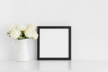 Siyah kare çerçeve, beyaz bir masadaki vazoda bir buket beyaz gül..