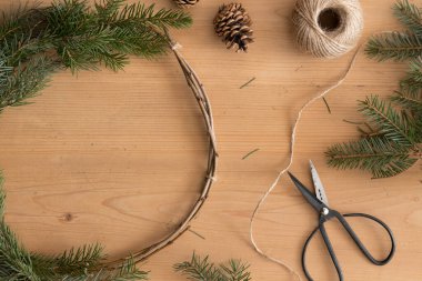 Tahta bir masanın üzerinde kozalaklı ve kozalaklı bir Noel çelengi yapıyorum..