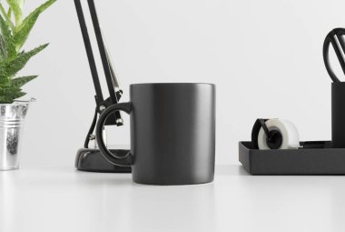 Siyah kupa, lamba, aloe vera bitkisi ve çalışma alanı aksesuarları beyaz bir masada..