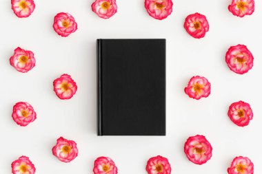 Beyaz arka planda pembe güller olan siyah bir kitap modelinin üst görüntüsü.