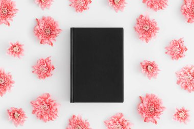 Beyaz arkaplanda pembe kasımpatı dekoru olan siyah bir kitap modelinin üst görüntüsü.