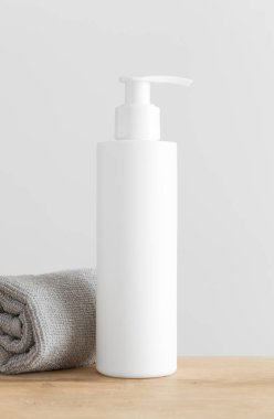 Beyaz kozmetik şampuan şişesi ahşap bir masada havluyla hazırlanıyor..